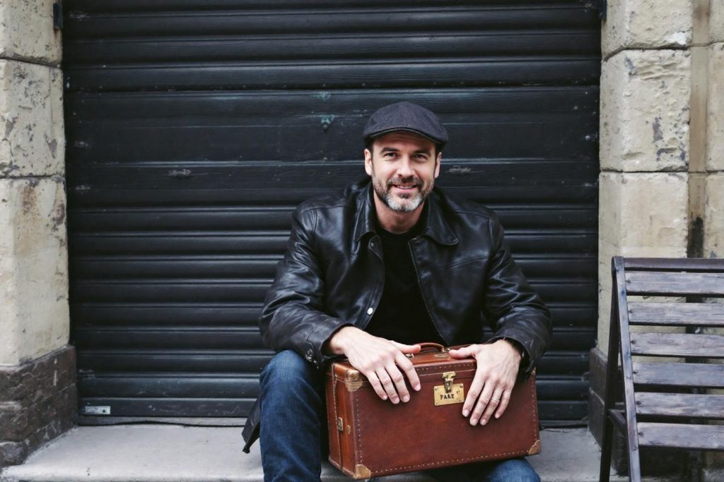 Homme à la veste en cuir assis sur un banc avec une valise
