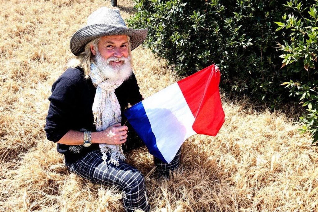 Homme âgé souriant portant un chapeau, tenant le drapeau français